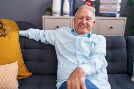 Téléchargez les photos : Moyen âge homme aux cheveux gris souriant confiant assis sur le canapé à la maison - en image libre de droit