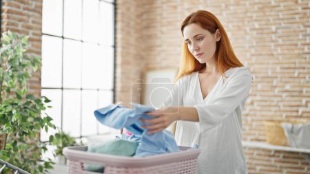 Photo for Young redhead woman hanging clothes on clothesline at laundry room - Royalty Free Image