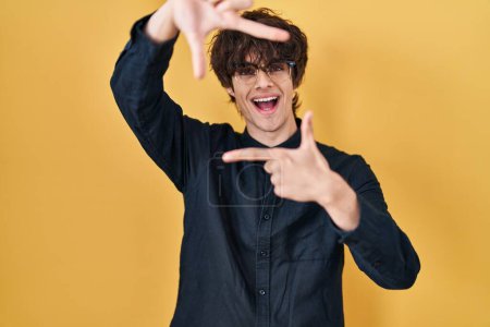 Photo for Young man wearing glasses over yellow background smiling making frame with hands and fingers with happy face. creativity and photography concept. - Royalty Free Image
