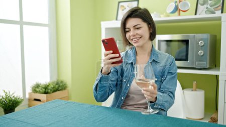Téléchargez les photos : Jeune femme caucasienne utilisant smartphone boire du vin à la maison - en image libre de droit