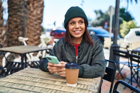 Photo for Young beautiful hispanic woman using smartphone drinking coffee at coffee shop terrace - Royalty Free Image
