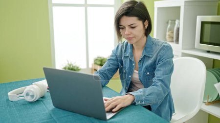 Foto de Mujer caucásica joven usando el ordenador portátil sentado en la mesa en casa - Imagen libre de derechos