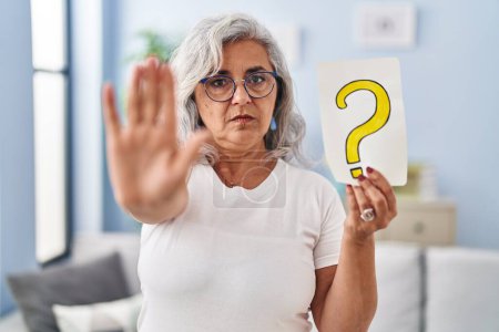 Photo for Middle age woman with grey hair holding question mark with open hand doing stop sign with serious and confident expression, defense gesture - Royalty Free Image