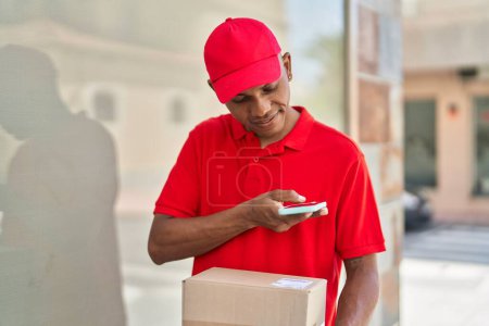 Photo for Young latin man delivery worker scanning package using smartphone at street - Royalty Free Image