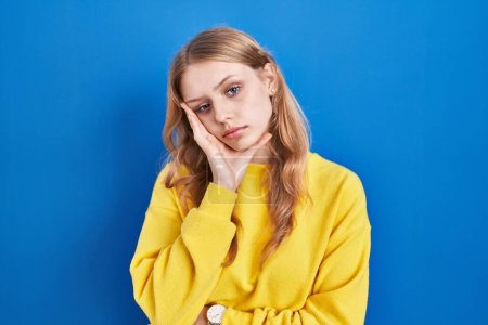 Foto de Young caucasian woman standing over blue background thinking looking tired and bored with depression problems with crossed arms. - Imagen libre de derechos