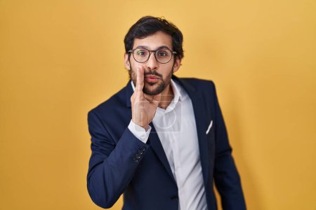 Photo for Handsome latin man standing over yellow background hand on mouth telling secret rumor, whispering malicious talk conversation - Royalty Free Image
