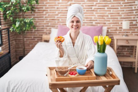 Téléchargez les photos : Jeune femme blonde en peignoir prenant le petit déjeuner dans la chambre - en image libre de droit