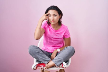 Photo for Hispanic young woman sitting on chair over pink background pointing unhappy to pimple on forehead, ugly infection of blackhead. acne and skin problem - Royalty Free Image
