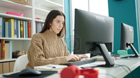 Téléchargez les photos : Jeune belle étudiante hispanique utilisant un ordinateur avec une expression sérieuse dans une salle de classe universitaire - en image libre de droit