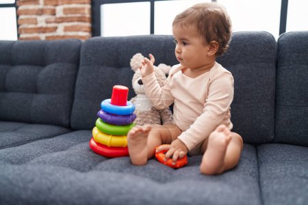 Téléchargez les photos : Adorable bébé hispanique jouant avec cerceaux jeu assis sur le canapé à la maison - en image libre de droit