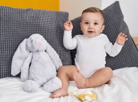 Téléchargez les photos : Adorable bébé caucasien souriant confiant assis sur le lit à la maison - en image libre de droit