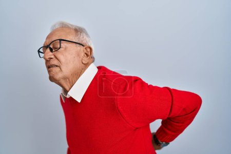 Foto de Hombre mayor con el pelo gris de pie sobre el fondo aislado sufriendo de dolor de espalda, tocando la espalda con la mano, dolor muscular - Imagen libre de derechos