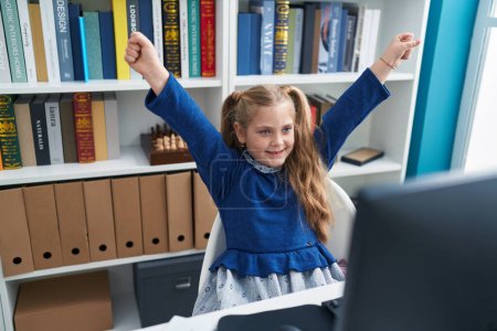 Téléchargez les photos : Adorable étudiante blonde utilisant un ordinateur avec expression gagnante en classe - en image libre de droit