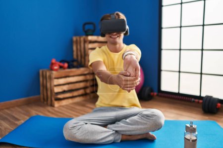Téléchargez les photos : Young caucasian man using virtual reality glasses stretching at sport center - en image libre de droit