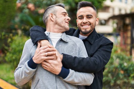 Foto de Dos hombres en pareja sonriendo confiados abrazándose en el parque - Imagen libre de derechos