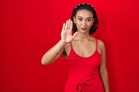 Photo for Young hispanic woman standing over red background doing stop sing with palm of the hand. warning expression with negative and serious gesture on the face. - Royalty Free Image