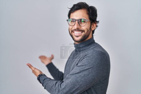 Foto de Hombre latino guapo de pie sobre un fondo aislado invitando a entrar sonriendo natural con la mano abierta - Imagen libre de derechos