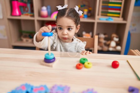 Téléchargez les photos : Adorable hispanique fille jouer avec cerceaux jouets assis sur la table à la maternelle - en image libre de droit