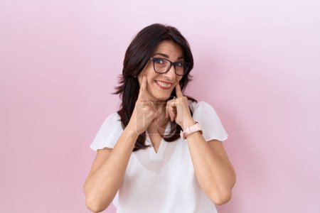 Téléchargez les photos : Femme hispanique du Moyen Âge portant un t-shirt blanc décontracté et des lunettes souriantes avec la bouche ouverte, les doigts pointant et forçant sourire joyeux - en image libre de droit