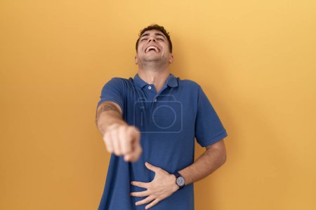 Téléchargez les photos : Jeune homme hispanique debout sur fond jaune se moquant de vous, pointant du doigt la caméra avec la main sur le corps, expression de honte - en image libre de droit