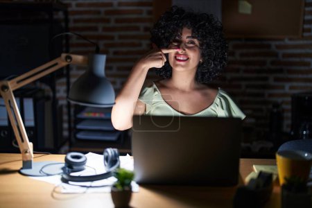Photo for Young brunette woman with curly hair working at the office at night pointing with hand finger to face and nose, smiling cheerful. beauty concept - Royalty Free Image