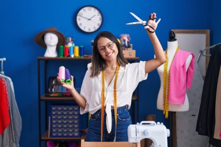 Photo for Young hispanic woman tailor smiling confident holding scissors and thread at sewing studio - Royalty Free Image