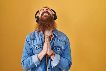 Photo for Caucasian man with long beard listening to music using headphones begging and praying with hands together with hope expression on face very emotional and worried. begging. - Royalty Free Image