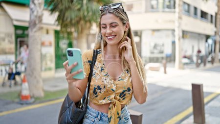 Téléchargez les photos : Jeune femme blonde souriant confiant en utilisant smartphone à la rue - en image libre de droit