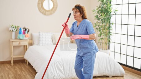 Photo for Middle age woman professional cleaner cleaning and dancing at bedroom - Royalty Free Image