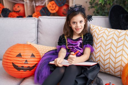 Photo for Adorable hispanic girl drawing on notebook having halloween party at home - Royalty Free Image