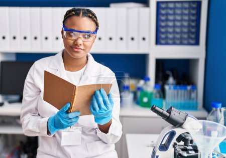 Photo for African american woman scientist reading book at laboratory - Royalty Free Image
