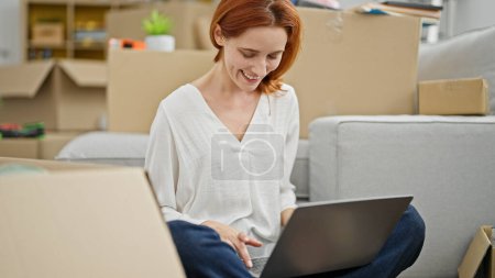 Foto de Mujer pelirroja joven usando el ordenador portátil sentado en el suelo en el nuevo hogar - Imagen libre de derechos