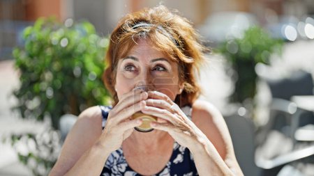 Téléchargez les photos : Femme d'âge moyen buvant du café assis sur la table à café terrasse - en image libre de droit