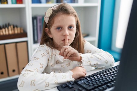 Photo for Adorable blonde girl student using computer doing silent gesture at classroom - Royalty Free Image