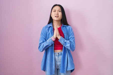 Photo for Young asian woman standing over pink background begging and praying with hands together with hope expression on face very emotional and worried. begging. - Royalty Free Image