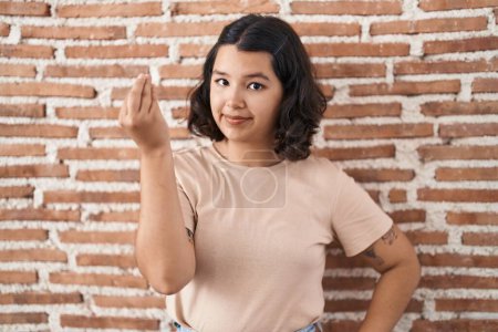 Photo for Young hispanic woman standing over bricks wall doing italian gesture with hand and fingers confident expression - Royalty Free Image