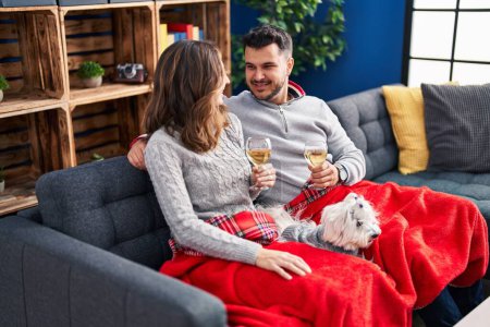 Foto de Man and woman toasting with champagne sitting on sofa with dog at home - Imagen libre de derechos