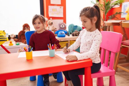 Foto de Adorables estudiantes de preescolar niñas sentados en el dibujo de la mesa en papel en el jardín de infantes - Imagen libre de derechos
