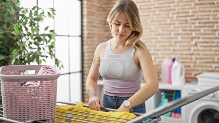 Téléchargez les photos : Young blonde woman hanging clothes on clothesline at laundry room - en image libre de droit