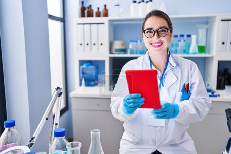Photo for Young beautiful hispanic woman scientist smiling confident using touchpad at laboratory - Royalty Free Image