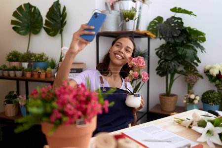 Photo for Young african american woman florist make selfie by smartphone holding plant at flower shop - Royalty Free Image