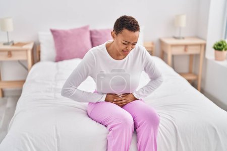 Photo for African american woman suffering for menstrual pain sitting on bed at bedroom - Royalty Free Image