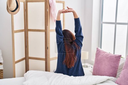 Téléchargez les photos : Jeune femme hispanique étirant les bras assis sur le lit dans la chambre - en image libre de droit