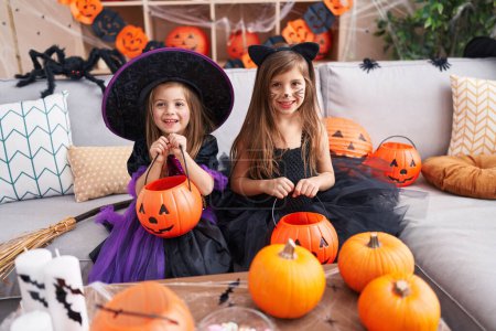 Téléchargez les photos : Adorables filles ayant fête d'Halloween tenant panier de citrouille à la maison - en image libre de droit