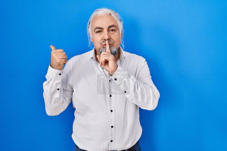 Photo for Middle age man with grey hair standing over blue background asking to be quiet with finger on lips pointing with hand to the side. silence and secret concept. - Royalty Free Image