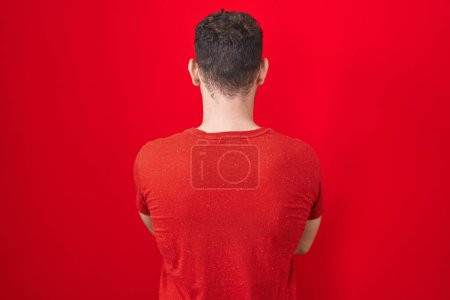 Téléchargez les photos : Young hispanic man standing over red background standing backwards looking away with crossed arms - en image libre de droit
