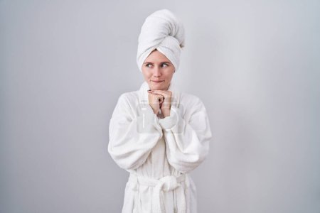 Photo for Blonde caucasian woman wearing bathrobe laughing nervous and excited with hands on chin looking to the side - Royalty Free Image