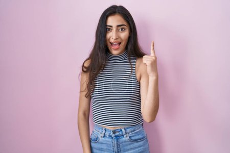 Téléchargez les photos : Jeune adolescente portant un t-shirt à rayures décontractées pointant du doigt avec une idée réussie. Sorti et heureux. numéro un. - en image libre de droit