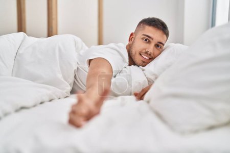 Téléchargez les photos : Jeune homme hispanique souriant confiant couché sur le lit dans la chambre - en image libre de droit