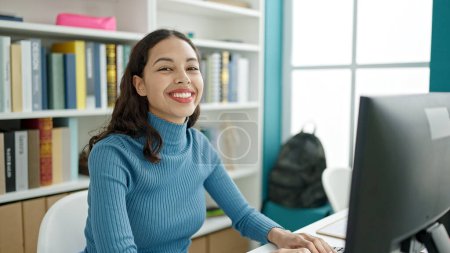 Téléchargez les photos : Jeune belle étudiante hispanique utilisant l'ordinateur souriant à la salle de classe universitaire - en image libre de droit